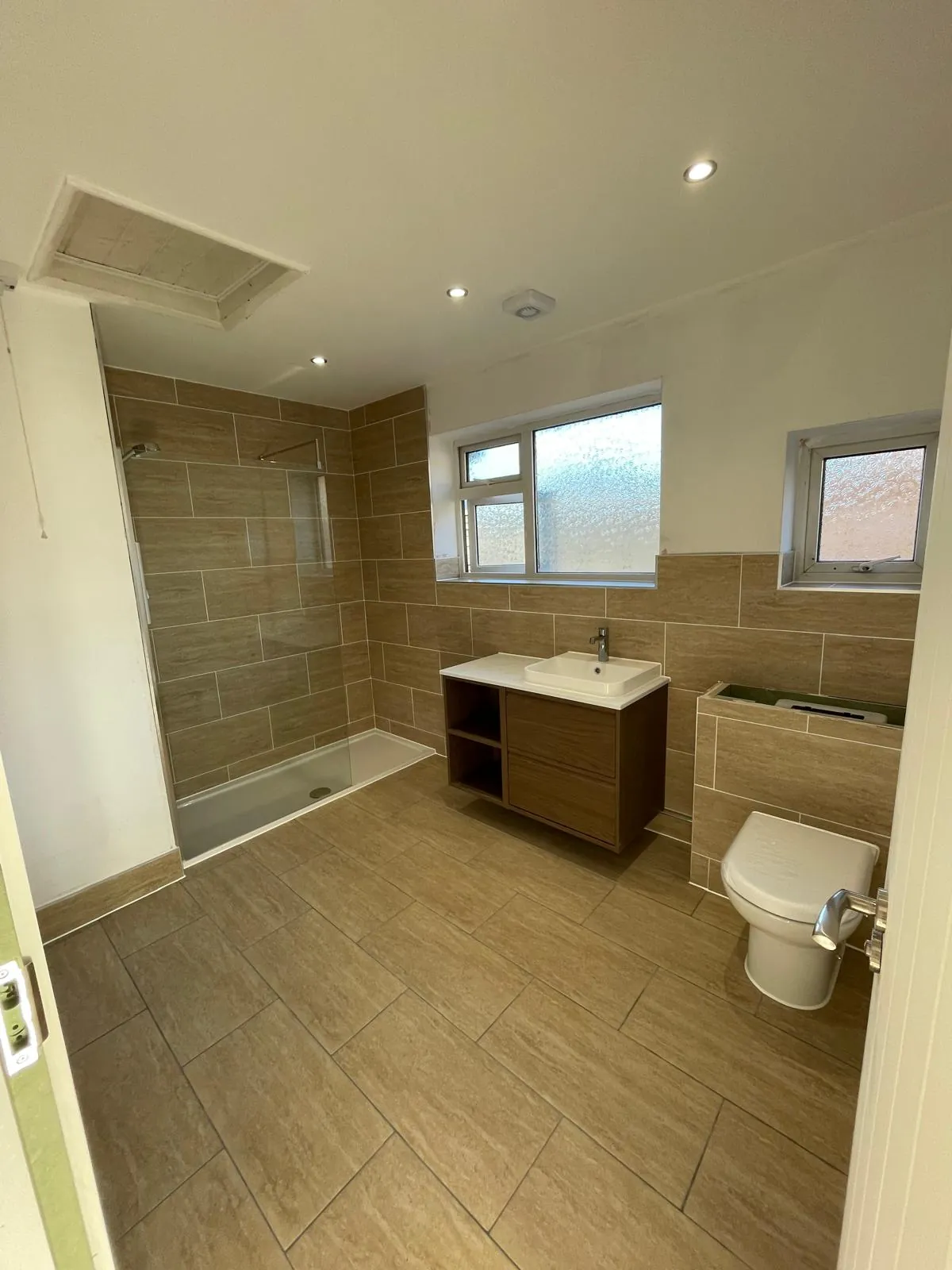 Newly tiled wet room with a walk-in shower and wall-hung vanity