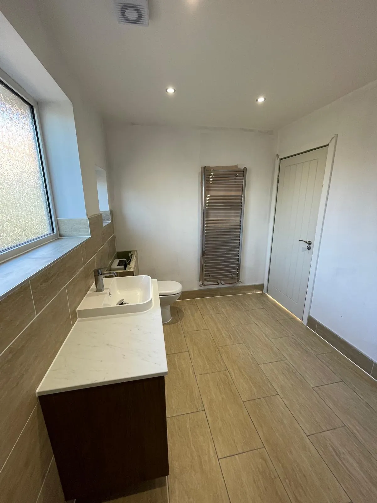 Refitted bathroom with wood-effect floor tiles and a chrome towel radiator